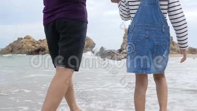 慢动作亚洲小女孩和妈妈一起在沙滩上与自然海浪海岸散步，为暑假提供概念